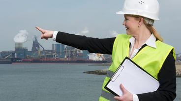 Female inspector in hardhat and safety vest pointing at industrial site