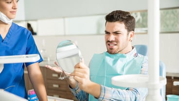 Mid adult man in pain looking at mirror while gesturing to female dentist in clinic