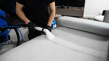 Cleaner is drycleaning sofa using extractor machine with detergent Using extractor to refresh and clean from dust and stains upholstered furniture