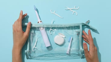 Cosmetic bag with toothbrush and dental floss in hands on blue background top view